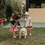 Two young girls joyfully playing with a fluffy dog in an outdoor park setting.