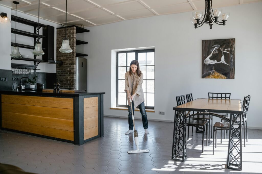 Woman mopping the floor in a contemporary kitchen and dining area with natural light.