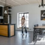 Woman mopping the floor in a contemporary kitchen and dining area with natural light.